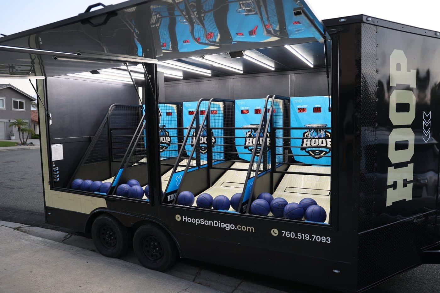 Side profile of the black Hoop San Diego arcade basketball trailer with cyan game panels